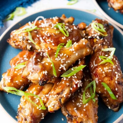 A plate of glazed chicken wings garnished with sesame seeds and sliced green onions, served on a blue dish.