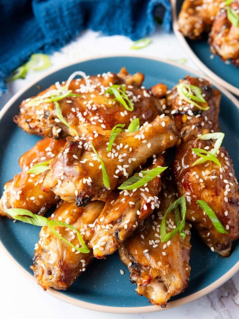 A plate of glazed chicken wings garnished with sesame seeds and sliced green onions, served on a blue dish.