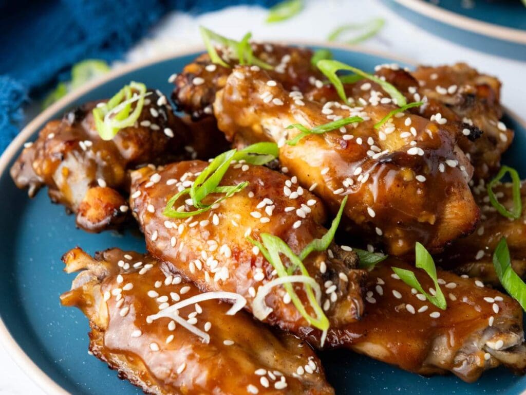 A plate of glazed chicken wings garnished with sesame seeds and sliced green onions.