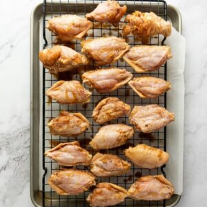 Raw, marinated chicken pieces arranged in rows on a wire rack over a baking sheet lined with parchment paper.