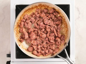 A frying pan filled with browned ground meat cooking on a stovetop.