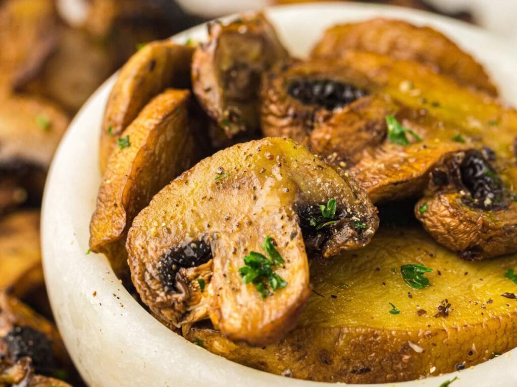Close-up of cooked, sliced mushrooms in a bowl, garnished with chopped parsley and seasoned with pepper.