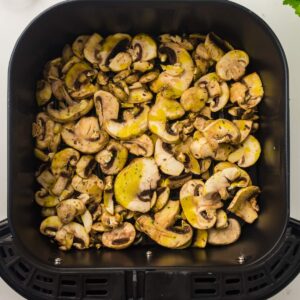 Sliced mushrooms coated in seasoning arranged in a single layer inside an air fryer basket, ready for cooking.