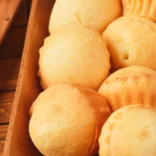 A wooden tray filled with several round, golden-brown baked cheese breads.