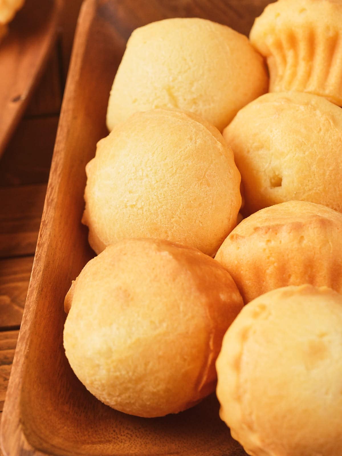 A wooden tray filled with several round, golden-brown baked cheese breads.