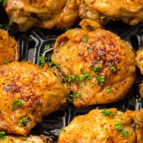 Close-up of several golden-brown, crispy chicken thighs garnished with chopped parsley, arranged on a black grill or air fryer tray.