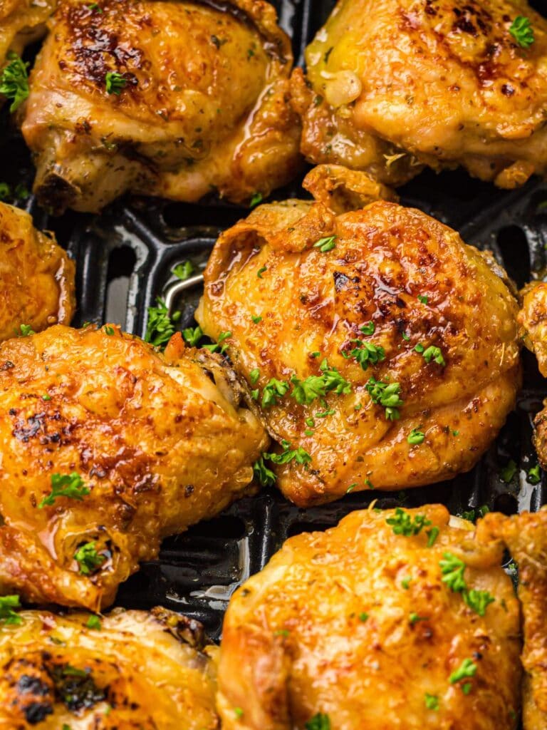 Close-up of several golden-brown, crispy chicken thighs garnished with chopped parsley, arranged on a black grill or air fryer tray.