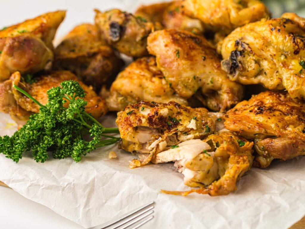 Golden-brown roasted chicken pieces with crispy skin and fresh parsley, served on parchment paper.