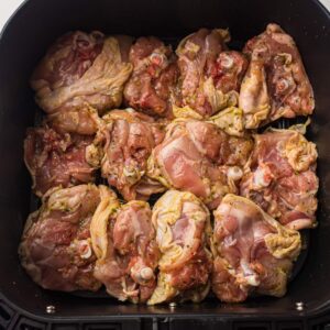 Raw, seasoned chicken thighs arranged in a single layer inside an air fryer basket, ready to be cooked.