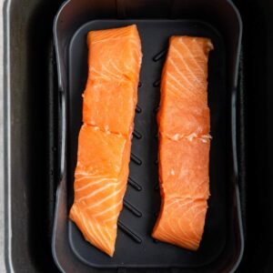 Two raw salmon fillets placed side by side on a black tray, ready to be cooked.