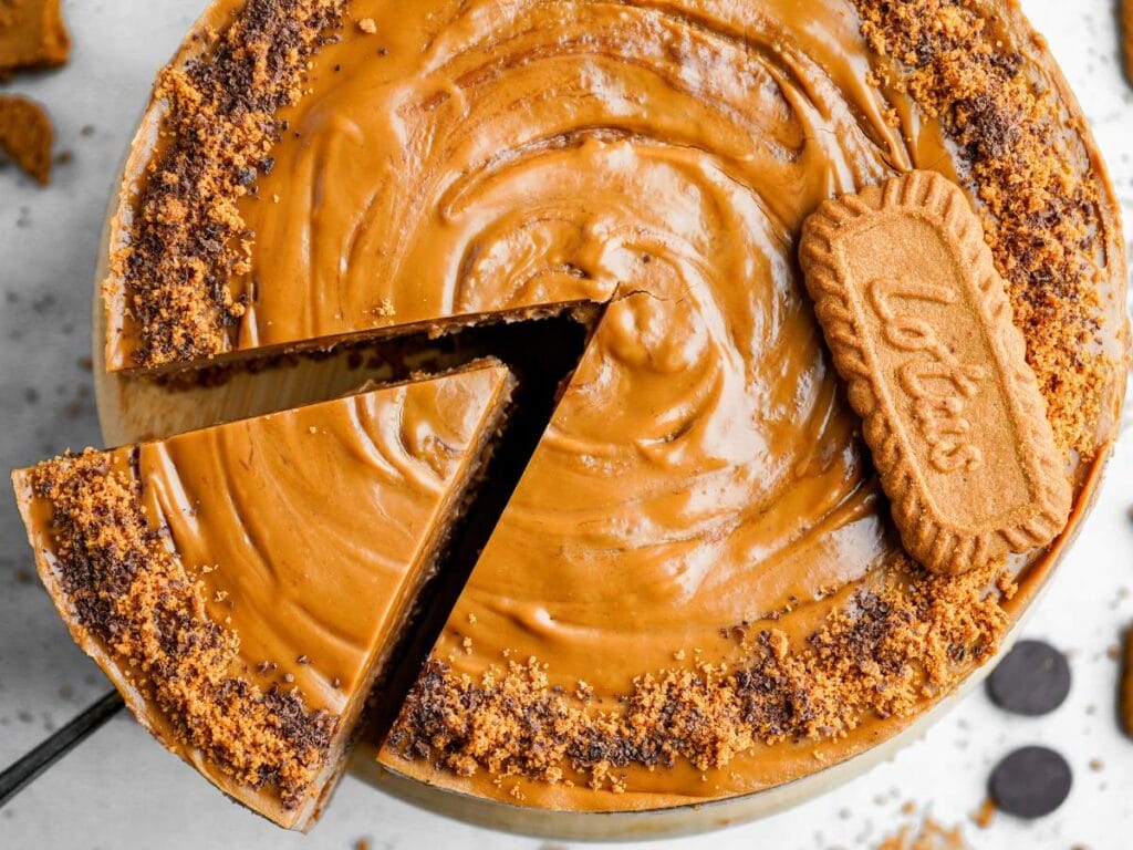 A cheesecake topped with smooth caramel-like Biscoff spread, a whole Lotus Biscoff cookie, and crushed cookie crumbs.