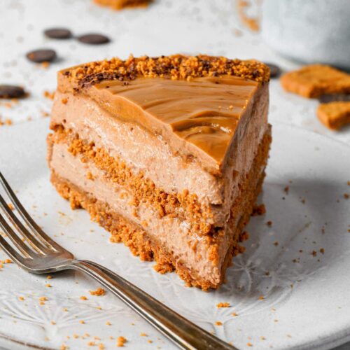 A slice of layered chocolate and caramel cake with a crumbly topping, served on a white plate with a fork.