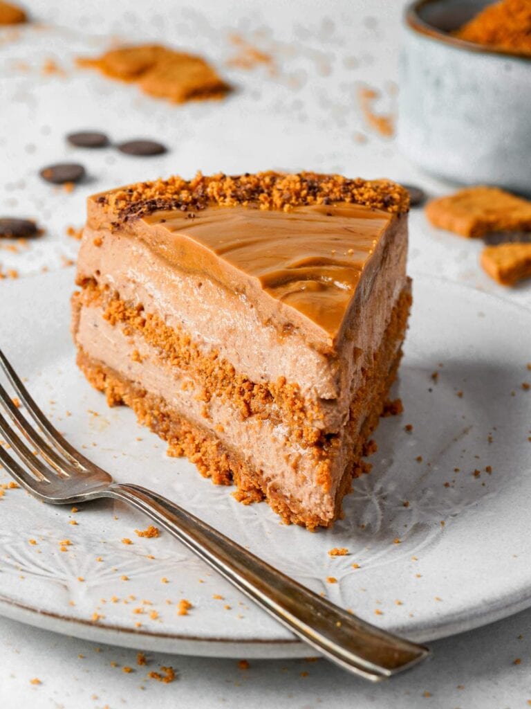 A slice of layered chocolate and caramel cake with a crumbly topping, served on a white plate with a fork.