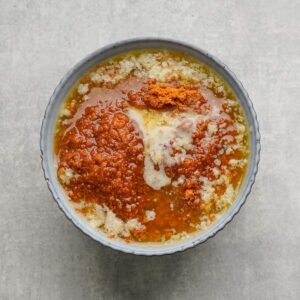 A bowl containing melted butter mixed with brown sugar, white sugar, and vanilla extract on a gray surface.