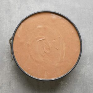 A round baking pan filled with smooth, light brown batter on a gray surface.