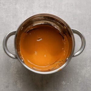 A stainless steel pot containing smooth, melted caramel sauce sits on a gray surface.