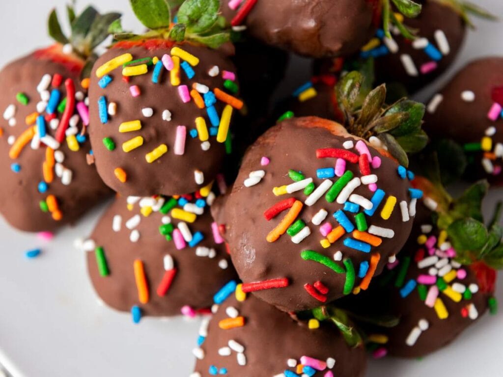 A plate of strawberries dipped in chocolate and topped with colorful rainbow sprinkles.