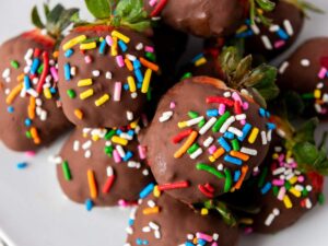 A plate of strawberries dipped in chocolate and topped with colorful rainbow sprinkles.