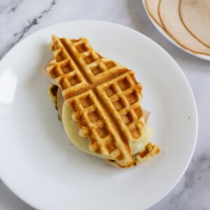 A sandwich made with waffles, sliced turkey, and melted cheese is served on a white plate.