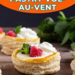 Three puff pastry vol-au-vent shells filled with cream and topped with whipped cream, raspberries, and mint leaves, displayed on a wooden surface.