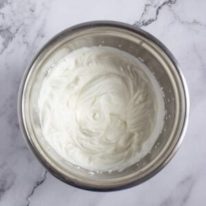A stainless steel bowl containing whipped cream on a white marble surface.