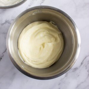 A stainless steel bowl filled with thick, creamy, pale yellow mixture, placed on a white marble surface.
