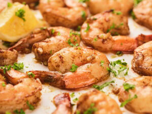 Close-up of cooked shrimp seasoned with herbs and spices, garnished with chopped parsley, with a lemon wedge in the background.