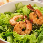 A bowl of fresh green lettuce topped with three grilled shrimp.