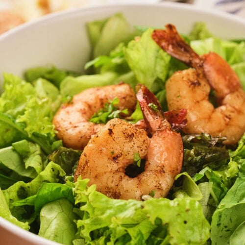 A bowl of fresh green lettuce topped with three grilled shrimp.