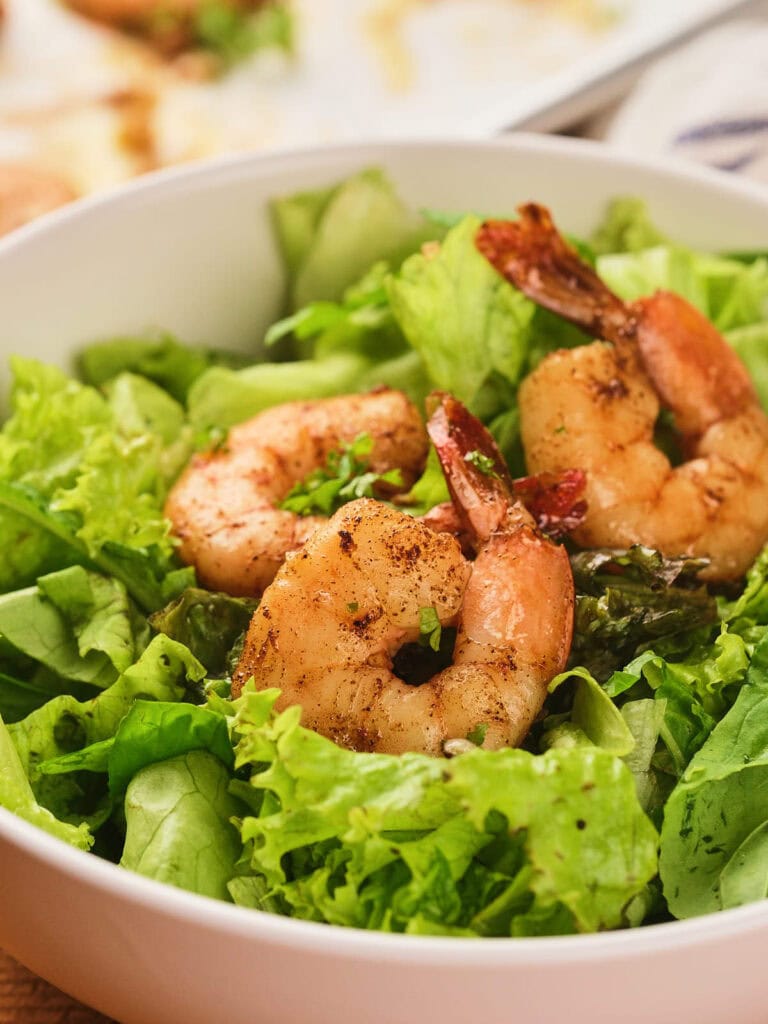 A bowl of fresh green lettuce topped with three grilled shrimp.