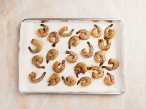 Raw marinated shrimp arranged in a single layer on a parchment-lined baking sheet.