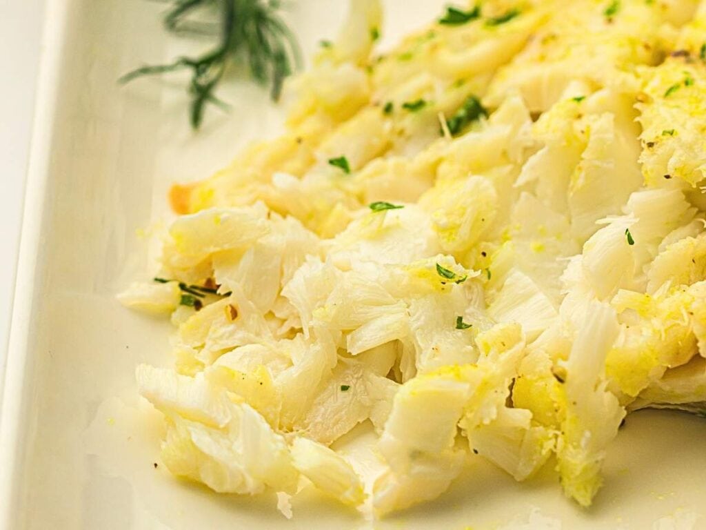 Shredded white fish garnished with chopped herbs on a white plate.
