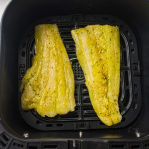 Two seasoned fish fillets placed side by side in the basket of an air fryer, ready to be cooked.
