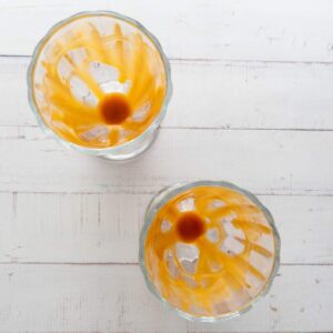 Top view of two empty glasses with caramel sauce remnants and a small puddle of liquid in each on a white wooden surface.