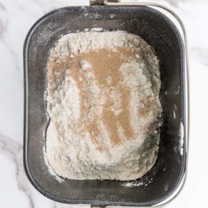 Bread machine pan containing flour and dry yeast, ready to be mixed for baking.