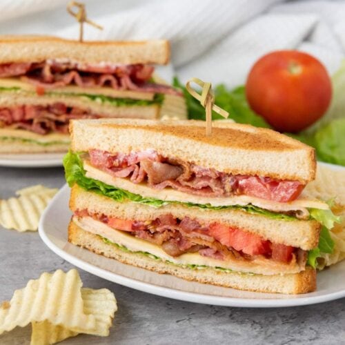 A BLT sandwich with bacon, lettuce, and tomato on toasted bread is sliced in half and served with potato chips on a white plate.