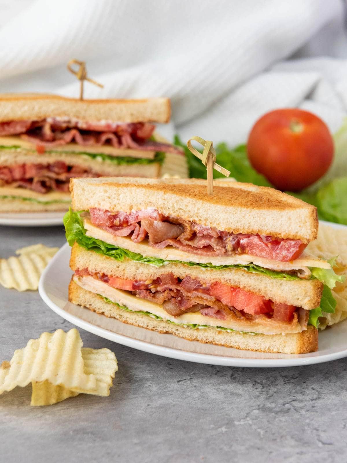 A BLT sandwich with bacon, lettuce, and tomato on toasted bread is sliced in half and served with potato chips on a white plate.