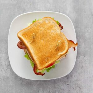 A BLT sandwich with bacon, lettuce, and tomato between toasted bread, secured with toothpicks, on a white plate.