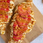 Two waffles topped with sliced strawberries, cream, crumbled cookie pieces, and a drizzle of caramel sauce on a wooden board.
