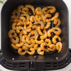 Raw, seasoned shrimp arranged in a single layer inside an air fryer basket, ready to be cooked.