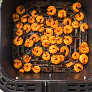 Seasoned shrimp arranged in a single layer inside an air fryer basket, cooked and slightly browned on the edges.