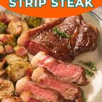 Plate with sliced New York strip steak cooked medium-rare, served with roasted Brussels sprouts and bacon pieces, garnished with a sprig of parsley.