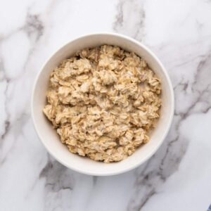A white bowl filled with cooked oatmeal sits on a white marble surface.