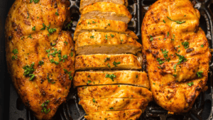 Three seasoned chicken breasts, one sliced, rest on a grill pan, garnished with chopped parsley.