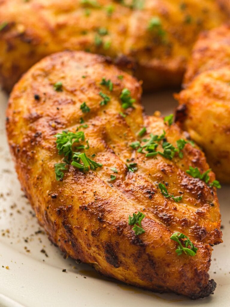 Grilled seasoned chicken breast garnished with chopped parsley sits on a white plate.