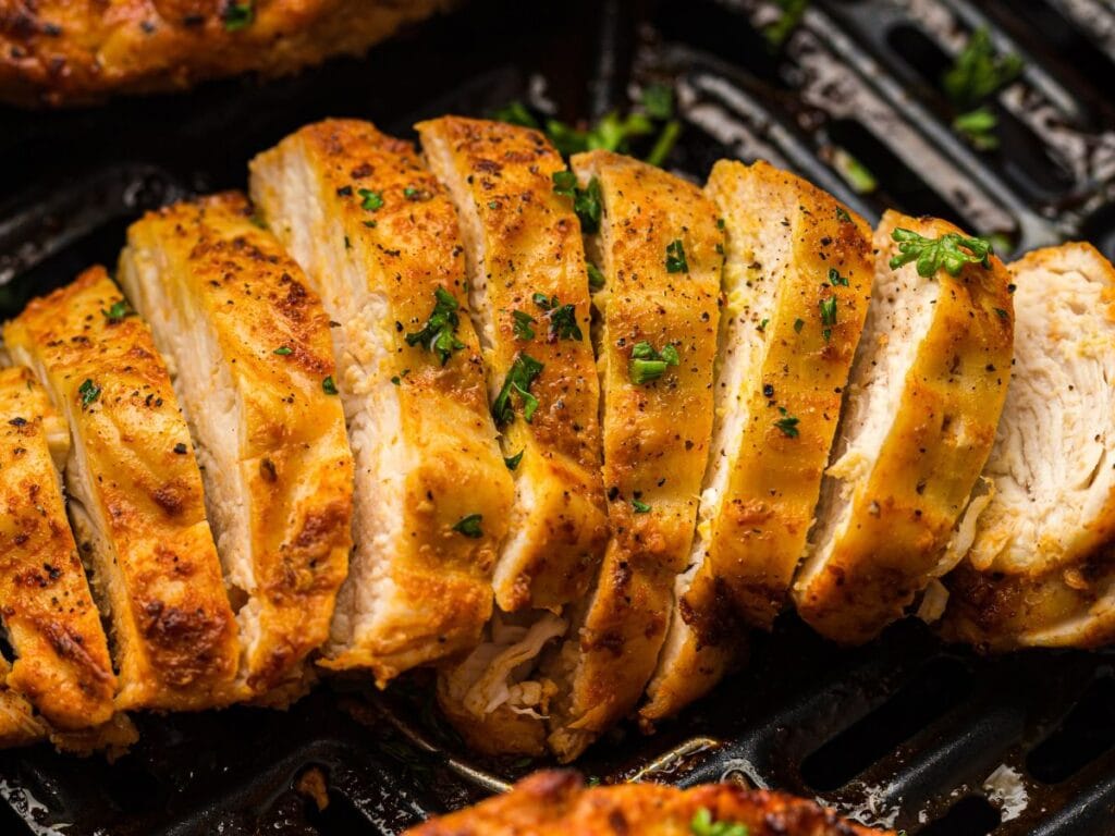 Sliced grilled chicken breast with golden-brown seasoning and chopped parsley, arranged on a grill pan.