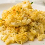 Macaroni and cheese topped with golden breadcrumbs and garnished with herbs on a white plate.