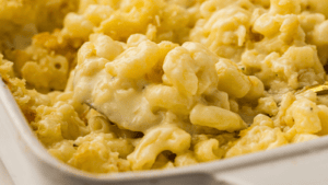 Close-up of creamy baked macaroni and cheese in a white dish, with a serving spoon lifting a portion.