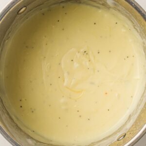 A close-up of creamy, light yellow sauce with visible black pepper specks in a metal pot.