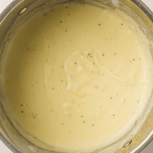 A close-up of creamy, light yellow sauce with visible black pepper specks in a metal pot.